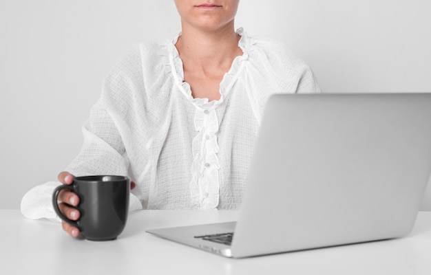 Personne sérieuse tenant une tasse à côté d'un ordinateur portable