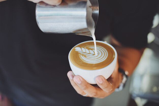 Personne servant une tasse de café avec une cruche de métal