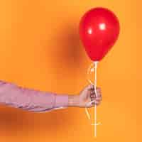 Photo gratuite personne tenant un ballon rouge sur fond orange