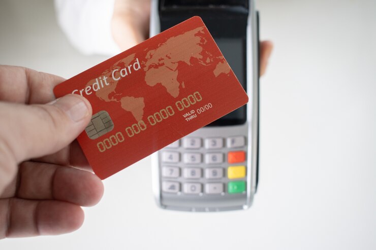 Photo gratuit personne tenant une carte de crédit rouge avec un terminal de paiement flou en arrière-plan