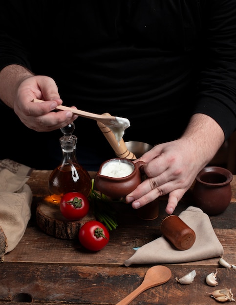 Une personne tenant un pot de yaourt dans les mains Tomates sur la table en bois