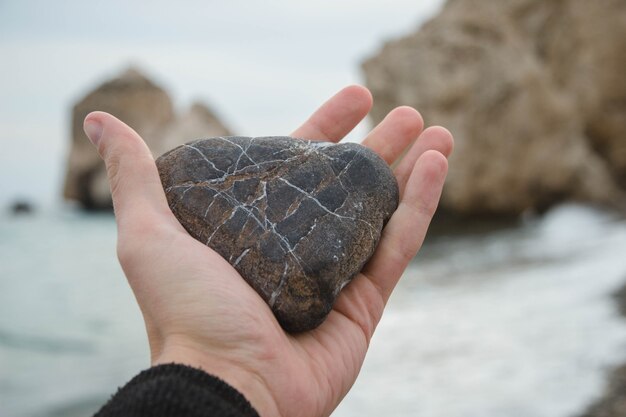 Personne tenant un rocher en forme de coeur dans ses mains sur la plage