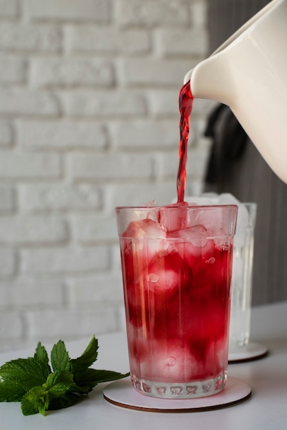 Personne versant du thé glacé à l'hibiscus rafraîchissant dans un récipient en verre transparent