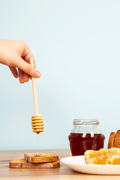 Une personne verse du miel sur une tranche de pain sur une table en bois