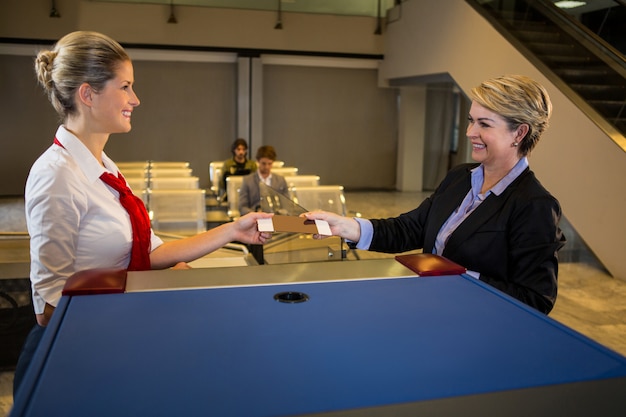 Photo gratuite personnel féminin donnant la carte d'embarquement à la femme d'affaires au comptoir