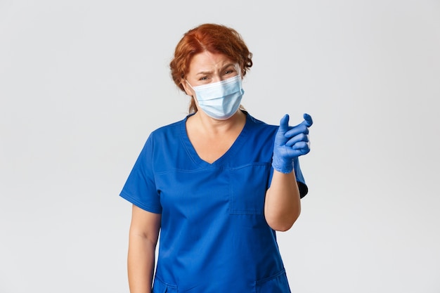 Personnel médical, pandémie, concept de coronavirus. Femme médecin, infirmière ou médecin déçue et se plaignant de montrer quelque chose de trop petit et d'avoir l'air mécontent, portez un masque facial et des gants.
