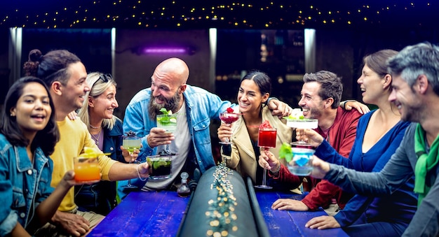 Personnes multiculturelles grillant des boissons fantaisie multicolores au bar à la mode