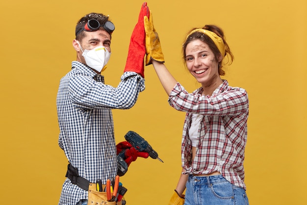 Photo gratuite personnes, profession, travail d'équipe, concept de coopération. caucasian couple debout sur le côté faisant des travaux de construction à la maison en touchant leurs mains ensemble se réjouissant de leur succès et d'excellents résultats