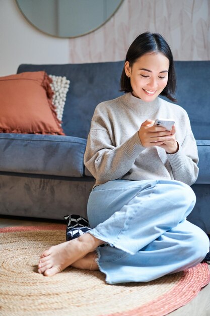 Personnes et technologie femme asiatique souriante assise à la maison à l'aide de son front de message de saisie de téléphone portable