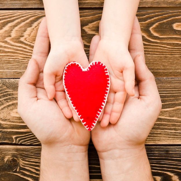 Photo gratuite personnes tenant un coeur rouge en mains sur fond de bois