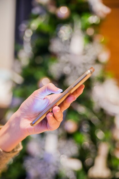 Personnes, vacances, communication, technologie et concept Internet - femme souriante avec des téléphones intelligents textuels à la maison sur fond d&#39;arbre de Noël, femme utilisant son téléphone mobile à la maison. Fond d&#39;écran de Noël Boke