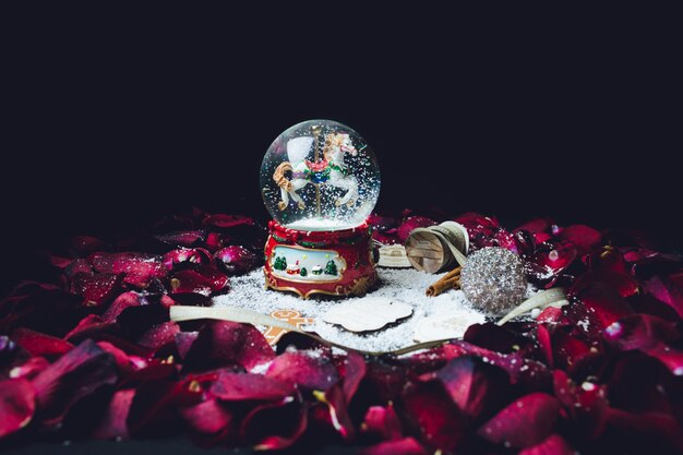 Les pétales de rose rouge entourent la boule de verre de Noël avec de la neige