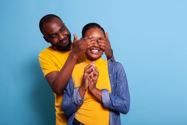 Petit ami joyeux couvrant les yeux de sa petite amie pour se préparer à la surprise, faisant un geste romantique avec un cadeau. Couple positif montrant de l'affection, étant amoureux. Les amoureux jouent à deviner qui.