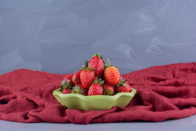 Petit bol de fraises niché sur un tas de nappe froissé sur fond de marbre.