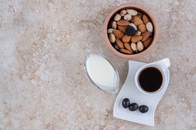 Un petit bol de lait à côté d'un bol de noix assorties et une tasse de café