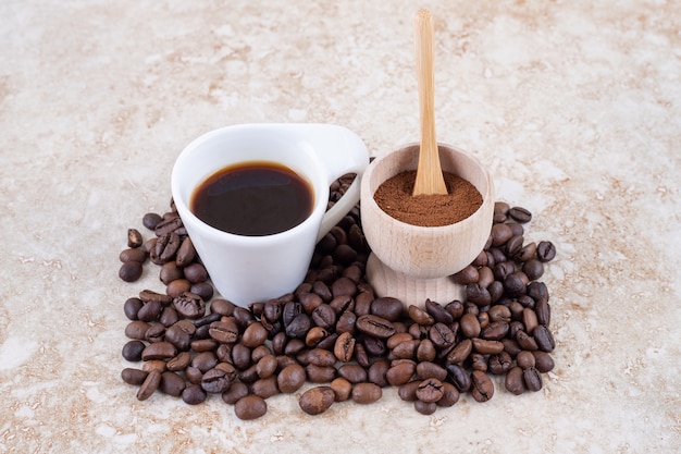 Un petit bol de poudre de café moulu et une tasse de café assis sur un tas de grains de café