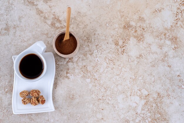 Un petit bol de poudre de café moulu, une tasse de café et des cacahuètes glacées