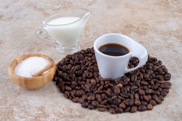 Petit bol de sucre à côté d'un tas de grains de café entourant une tasse de café