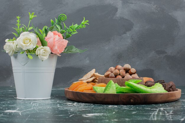 Petit bouquet avec assiette en bois de fruits secs sur mur de marbre.