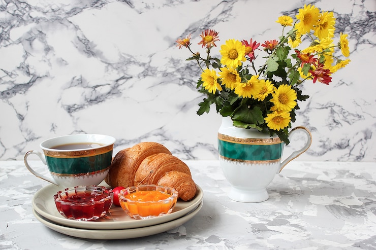 Photo gratuit petit déjeuner français avec croissants, confiture d'abricot, confiture de cerise et une tasse de thé, fleurs rouges et jaunes