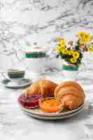 Photo gratuite petit déjeuner français avec croissants, confiture d'abricot, confiture de cerise et une tasse de thé, fleurs rouges et jaunes