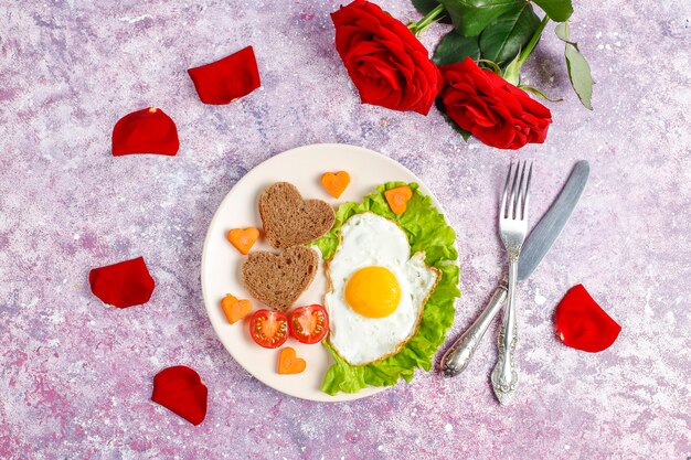 Petit-déjeuner le jour de la Saint-Valentin - œufs au plat et pain en forme de cœur et légumes frais.