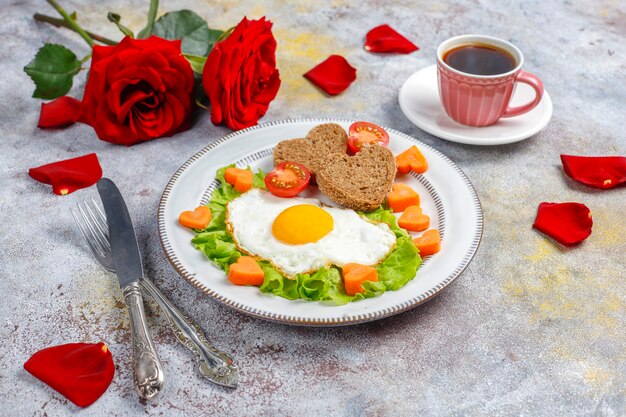 Petit-déjeuner le jour de la Saint-Valentin - œufs au plat et pain en forme de cœur et légumes frais.