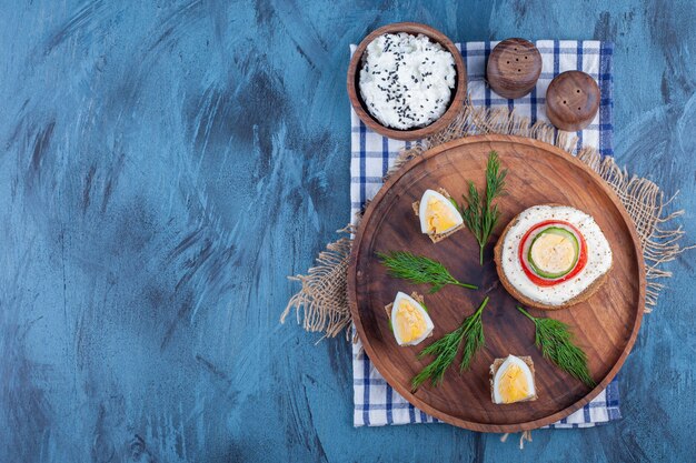 Un petit-déjeuner léger sur une plaque en bois sur des morceaux de tissu sur fond bleu.