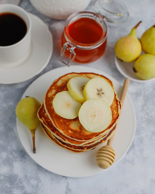 Petit déjeuner maison: pancakes de style américain servis avec des poires et du miel avec une tasse de thé sur du béton. Vue de dessus et copie