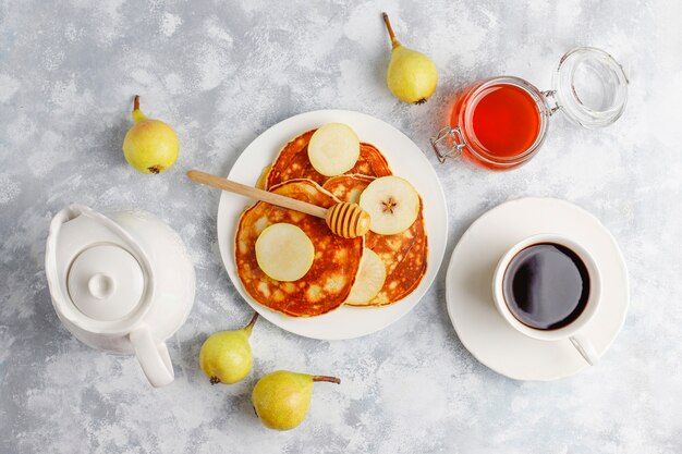 Petit déjeuner maison: pancakes de style américain servis avec des poires et du miel avec une tasse de thé sur du béton. Vue de dessus et copie