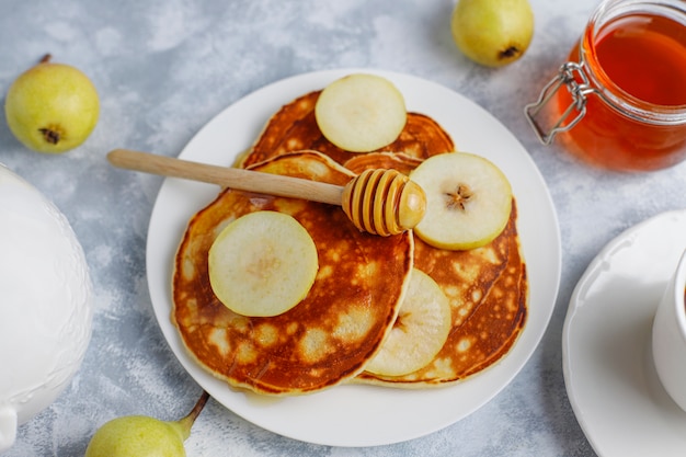 Petit déjeuner maison: pancakes de style américain servis avec des poires et du miel avec une tasse de thé sur du béton. Vue de dessus et copie