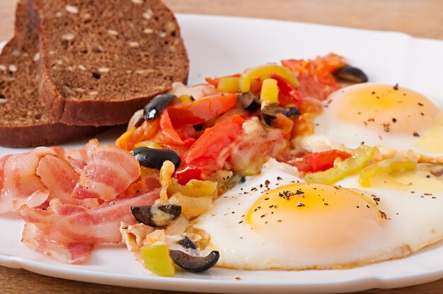 Petit déjeuner - œufs au plat avec bacon, tomates, olives et tranches de fromage