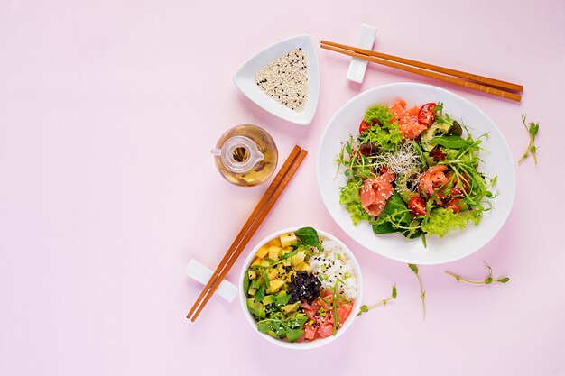 Petit-déjeuner sain. Bol de Bouddha avec riz, mangue, avocat et saumon et salade fraîche aux tomates, avocat, roquette, graines, saumon. Concept d'aliments sains. Vue de dessus. Mise à plat