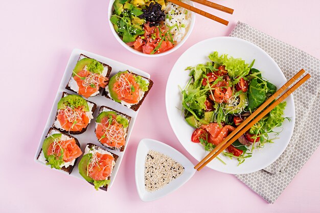 Petit-déjeuner sain. Bol de Bouddha avec riz, mangue, avocat et saumon et salade fraîche aux tomates, avocat, roquette, graines, saumon et sandwich au saumon avec avocat, fromage creame et micro-vert. Healt