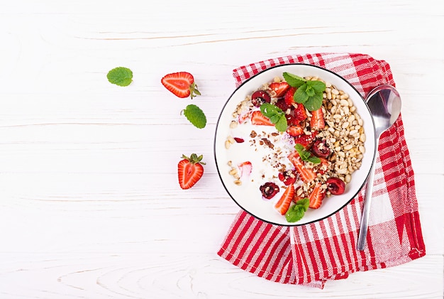 Petit-déjeuner sain - granola, fraises, cerise, noix et yaourt dans un bol sur une table en bois. Concept alimentaire végétarien. Vue de dessus