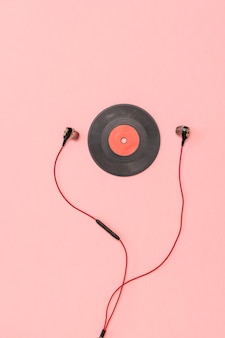 Un petit disque vinyle rouge et un casque sur fond rose. technique rétro pour jouer de la musique.