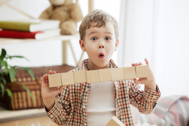 Petit enfant assis par terre. Garçon surpris assez souriant jouant avec des cubes en bois à la maison. Image conceptuelle avec copie ou espace négatif et maquette pour votre texte.