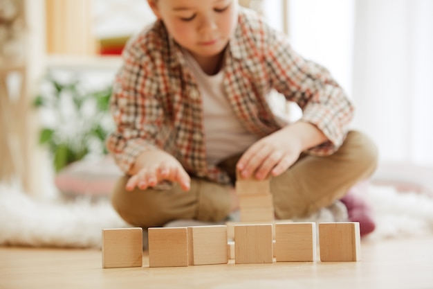 Petit enfant assis sur le sol. Joli garçon palying avec des cubes en bois à la maison. Image conceptuelle avec copie ou espace négatif et maquette pour votre texte