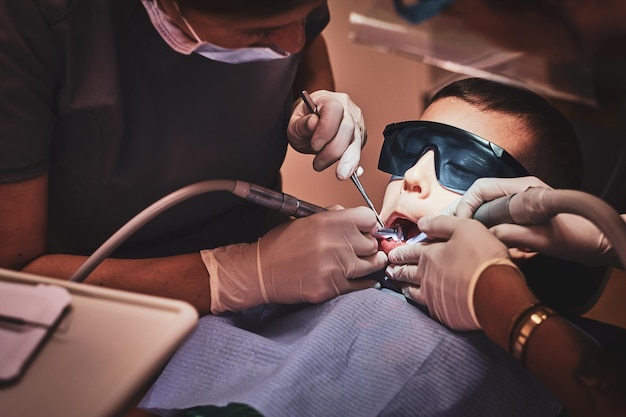 Photo gratuite un petit enfant courageux reçoit un traitement dentaire par un médecin expérimenté à la clinique dentaire.