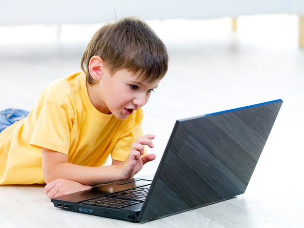 Petit enfant curieux avec ordinateur portable sur le sol - à l'intérieur