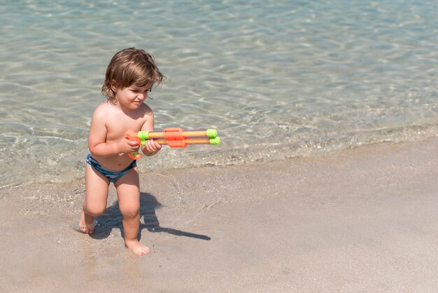 Petit enfant jouant avec un pistolet à eau sur la plage