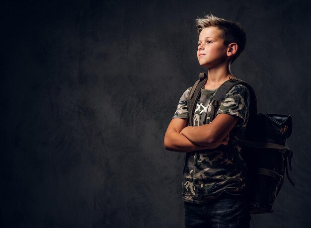 Un petit enfant pensif se tient dans un studio photo sombre tout en posant pour le photographe.