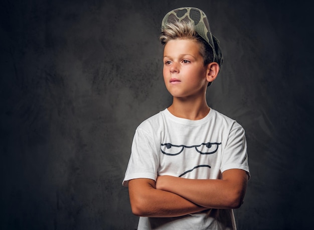 Un petit enfant pensif se tient dans un studio photo sombre tout en posant pour le photographe.