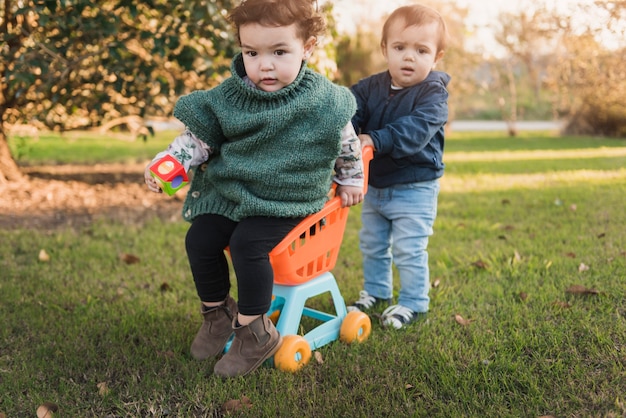 Petit frère et soeur jouant avec chariot de jouet dans le jardin