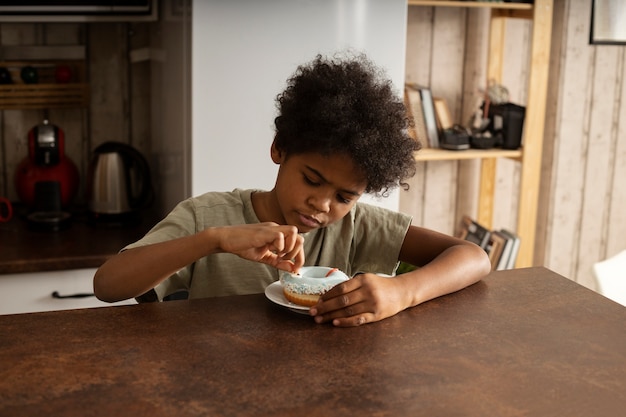 Photo gratuite petit garçon ayant un beignet dans la cuisine