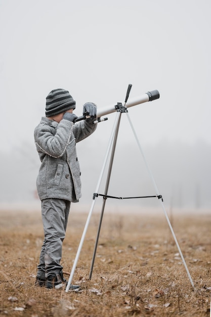 Photo gratuite petit garçon sur le côté à l'aide d'un télescope