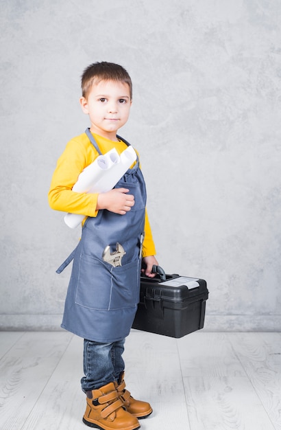 Petit garçon debout avec une boîte à outils et des rouleaux de papier