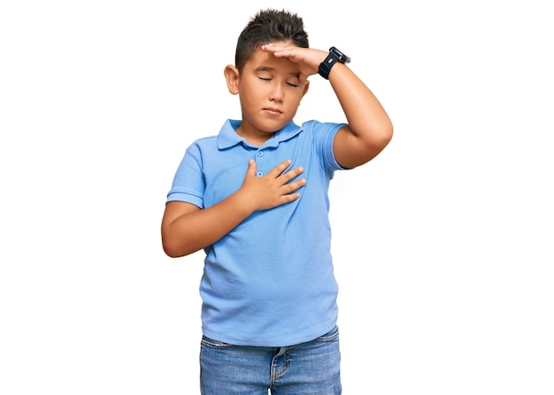 Petit garçon enfant hispanique portant des vêtements décontractés touchant le front pour la maladie et la fièvre, la grippe et le rhume, le virus malade