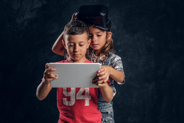 Le petit garçon et la fille se concentrent sur la tablette, la fille a des lunettes vr sur la tête.