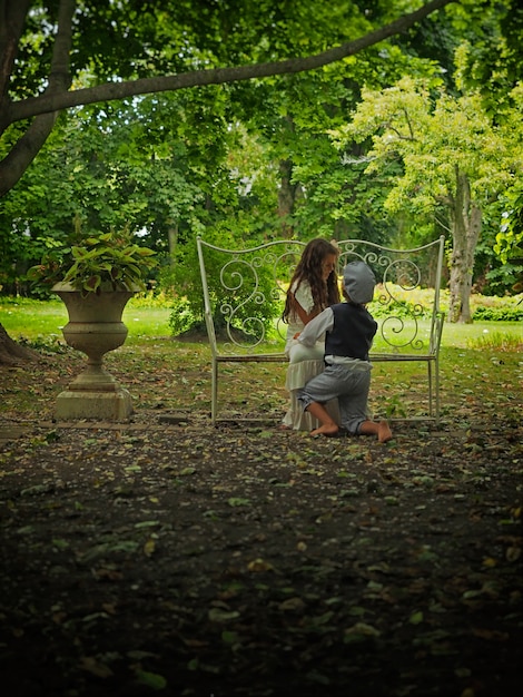 Petit garçon à genoux devant une petite fille dans un jardin entouré de verdure